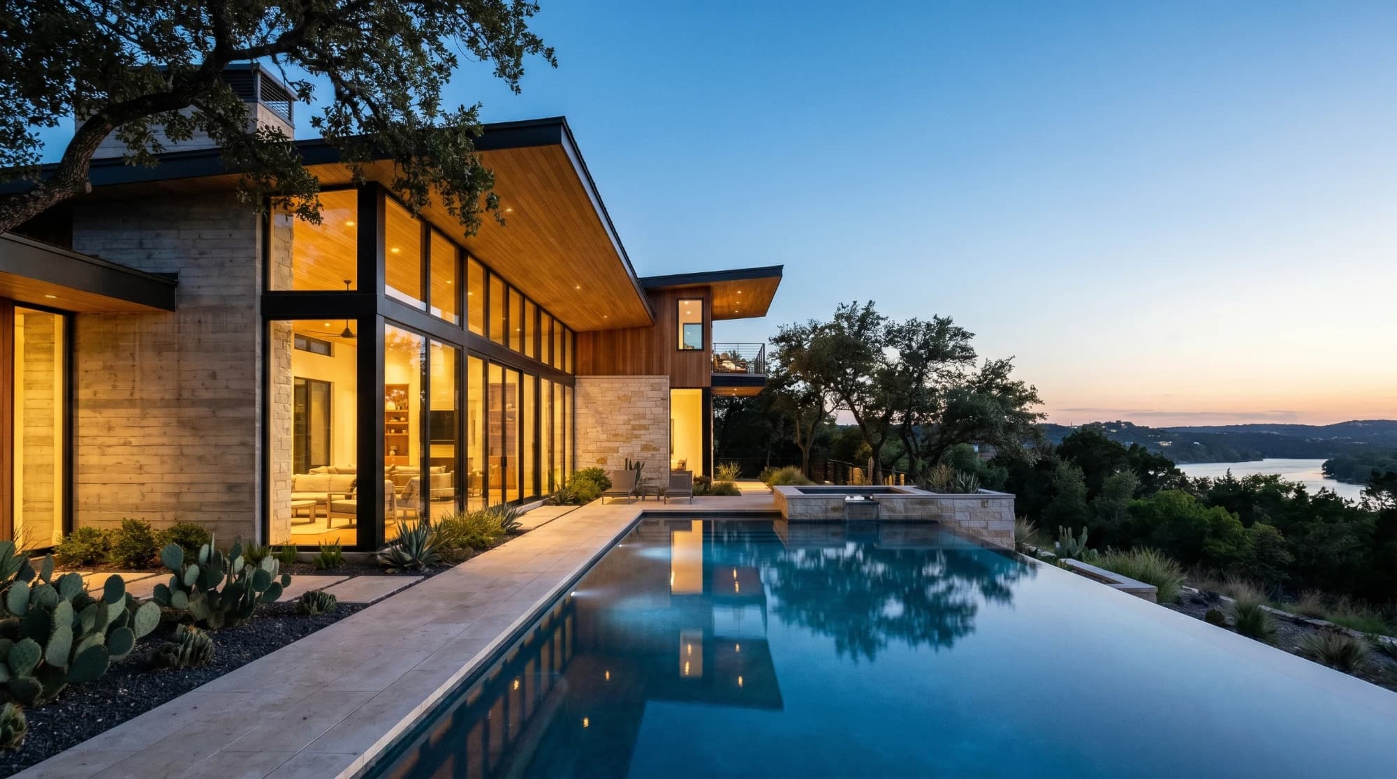 A modern two-story home at blue hour, its windows lit warm above an infinity pool